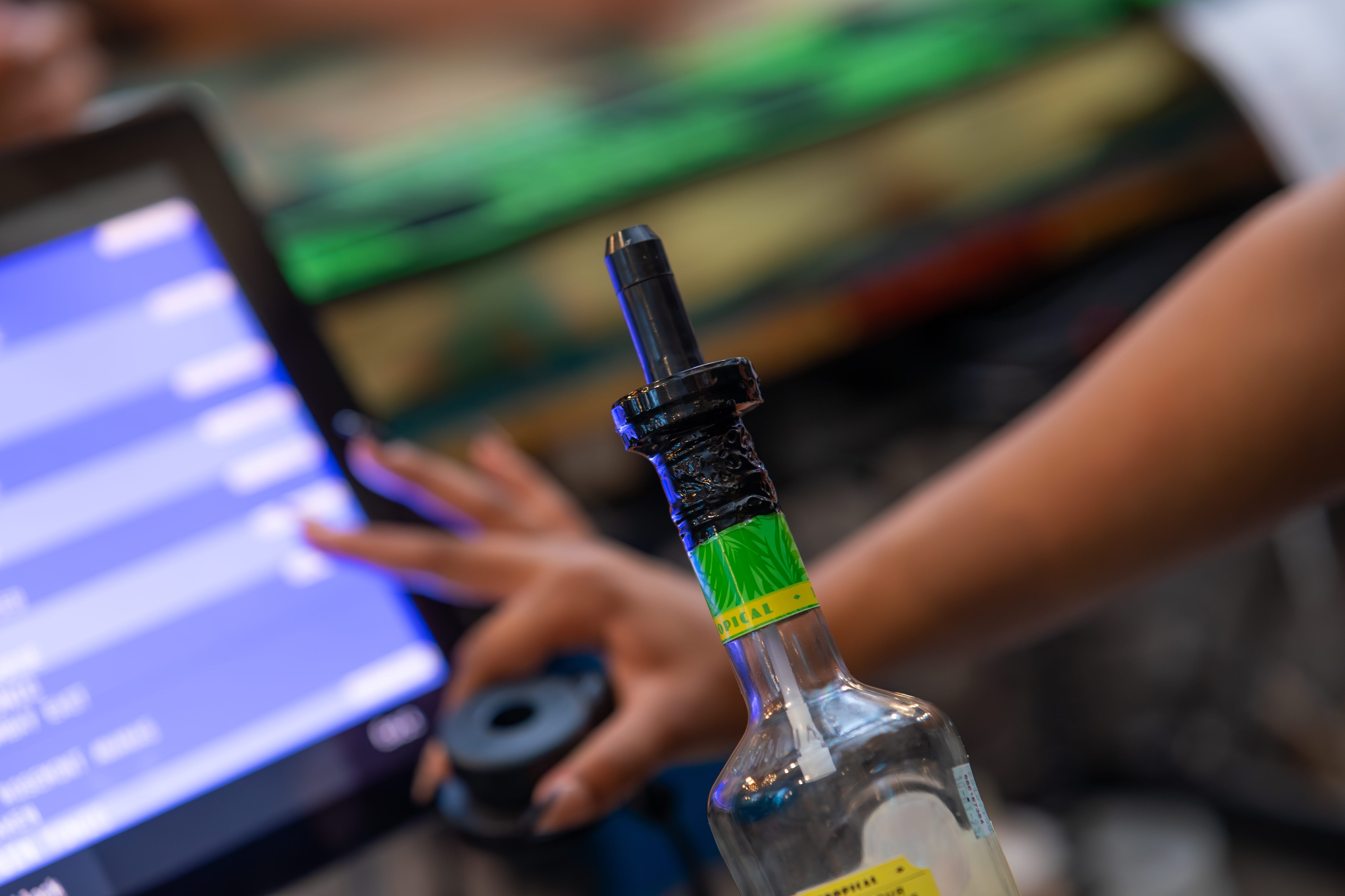 The VelMix system in action with its handheld device connected to a bottle, monitored through an integrated POS interface in the background.