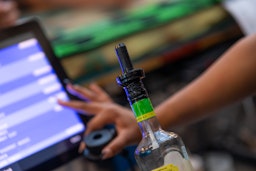 The VelMix system in action with its handheld device connected to a bottle, monitored through an integrated POS interface in the background.